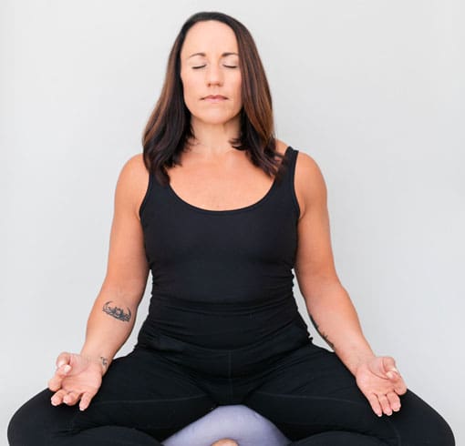 Jess Beran, Charleston SC intuitive life coach and Reiki practitioner, seated in meditation with eyes closed, practicing mindfulness and energy healing in a calm, minimalist setting.
